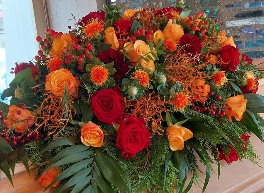 Üppiges Gesteck in Orange und Rot mit Rosen, Beeren und Nadelgrün